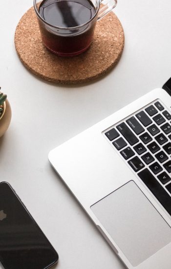 space gray iPhone X beside turned on laptop beside coffee and succulent plant